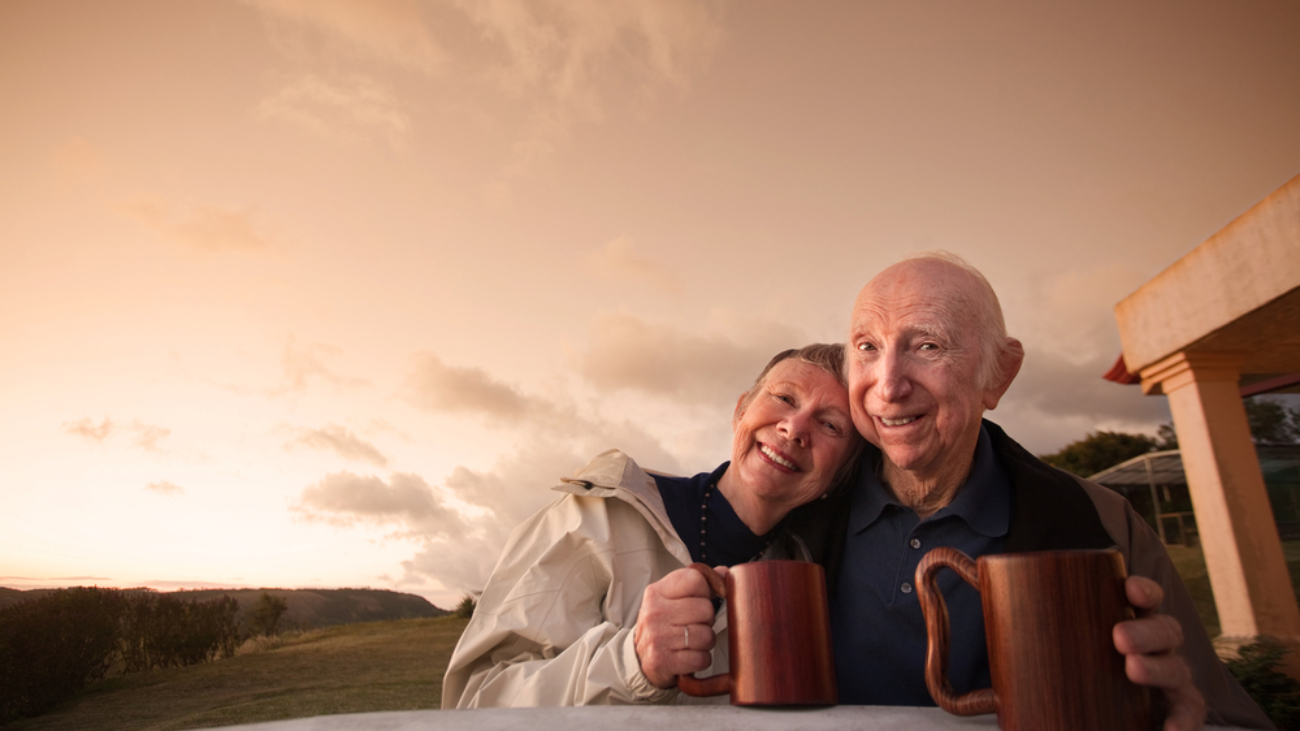 An elderly couple drinks coffee in their backyard