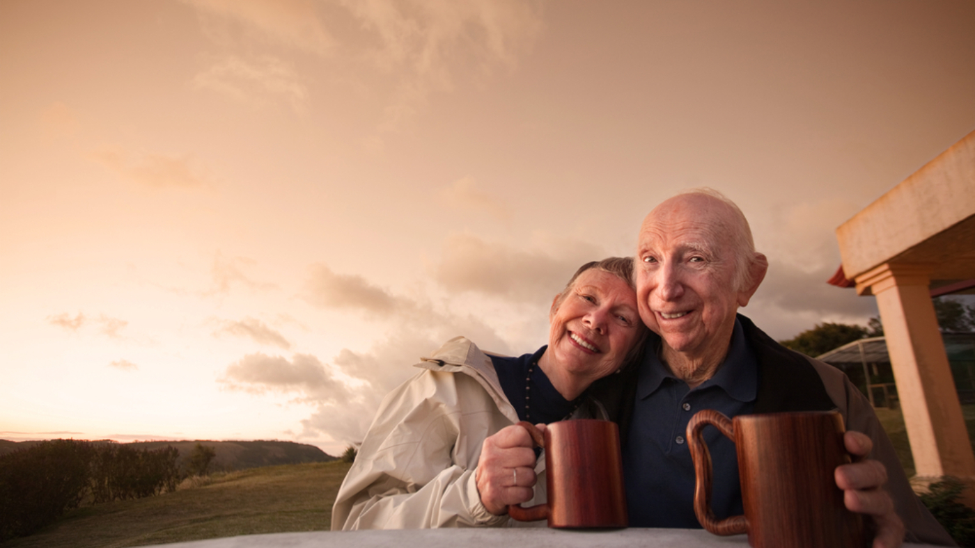 An elderly couple drinks coffee in their backyard